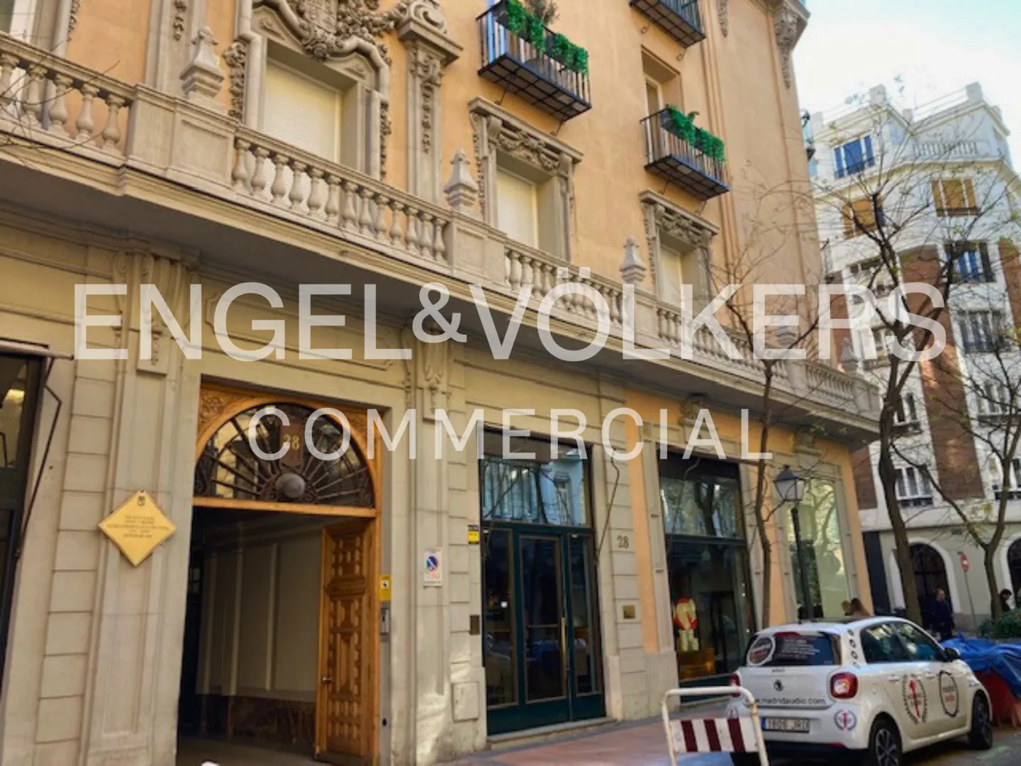 Exterior view of Engel & Volkers Commercial office in a beige building with balconies and a white car parked outside.