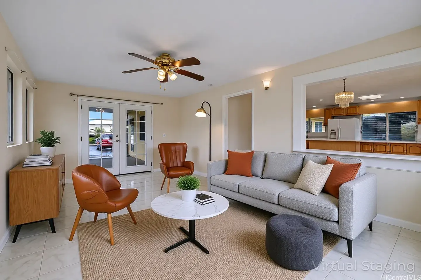 A bright living room with a gray sofa, brown leather chairs, and a white marble table on a tan rug. French doors lead outside.