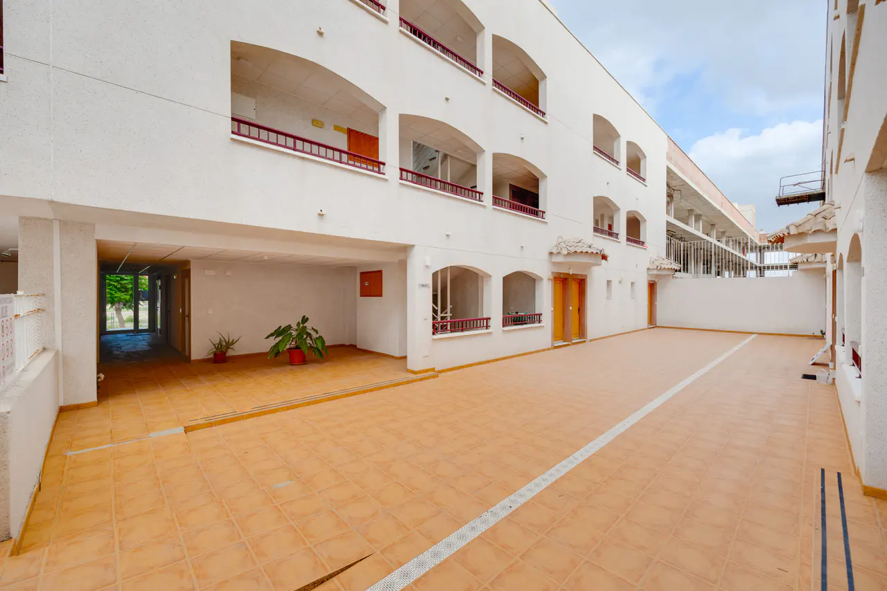 Exterior of a white building with arched balconies and a tiled courtyard. Plants are visible near an open garage area.