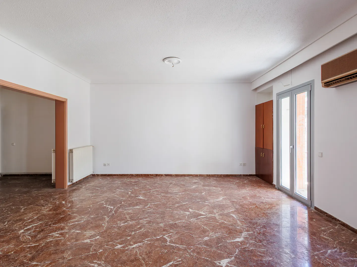 Empty room with white walls, red marble floor, and a door to another room. A closet and a glass door are on the right.