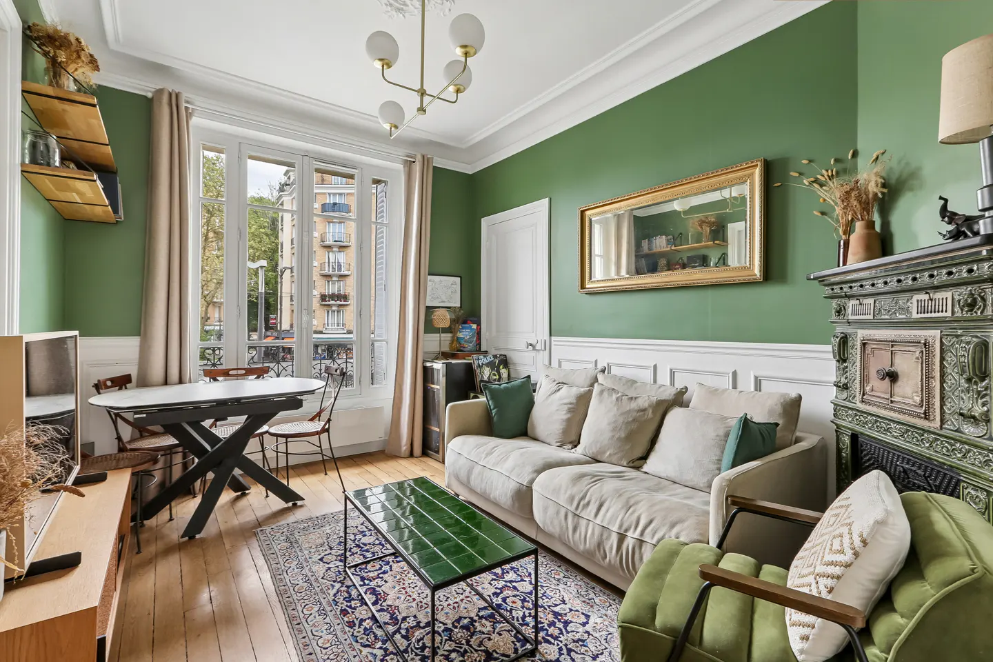 Living room with green walls, a beige sofa, and a green armchair. A window overlooks a city street.