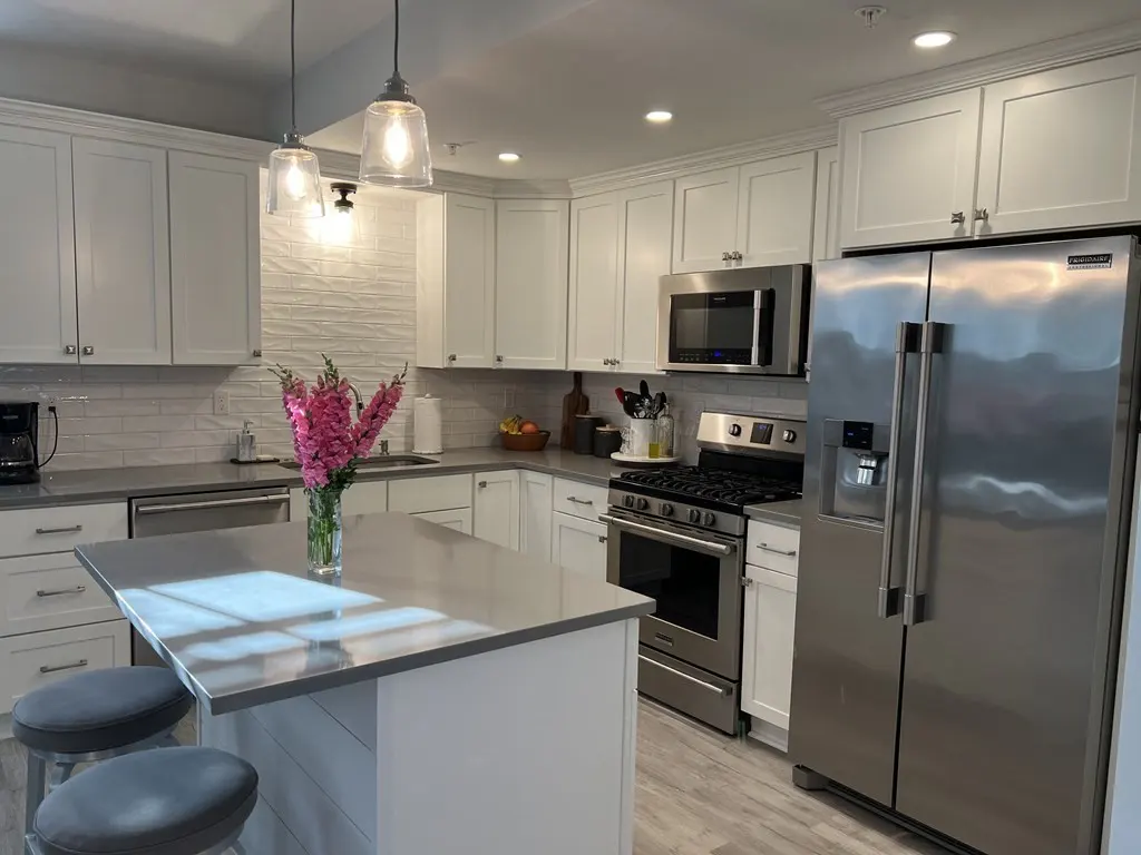 Bright kitchen with white cabinets, stainless steel appliances, and a gray island with two stools. Pink flowers in a vase add a pop of color.