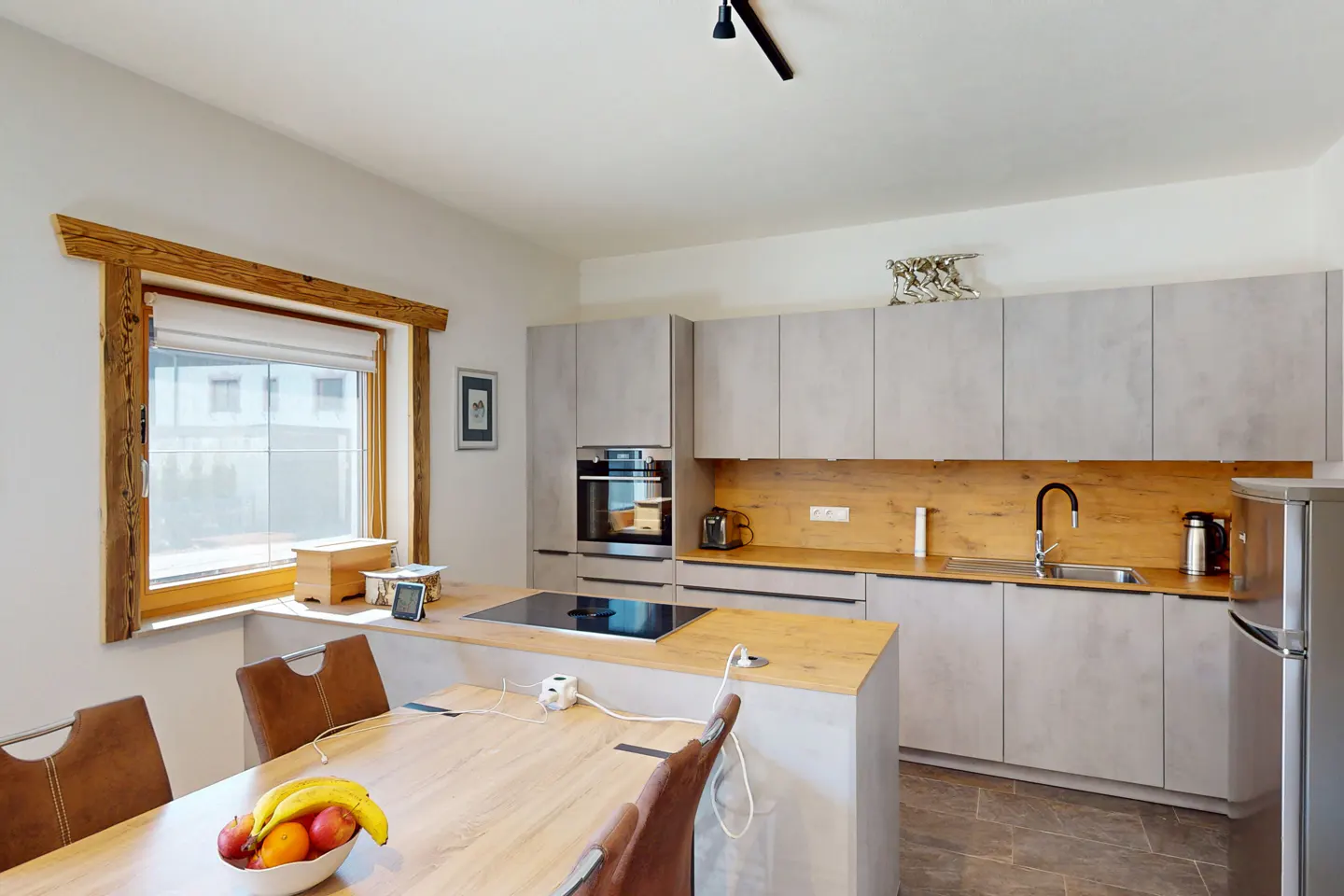 Bright kitchen with gray cabinets, wood countertops, and island. A bowl of fruit sits on the wood table near a window with a wood frame.