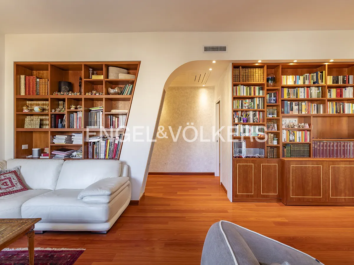 Living room with hardwood floors, built-in bookshelves filled with books, and a white sofa. An arched doorway leads to another room.