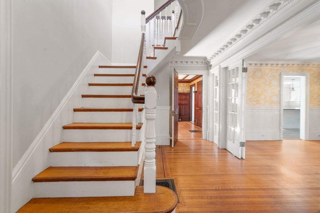 Staircase with wooden treads and white risers, leading to a hallway with hardwood floors and white paneled walls. [AI-generated text]