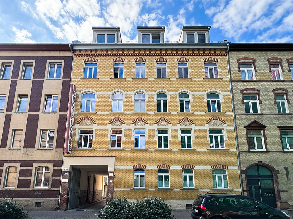 Exterior view of a yellow brick apartment building with white-framed windows and a car parked in front.