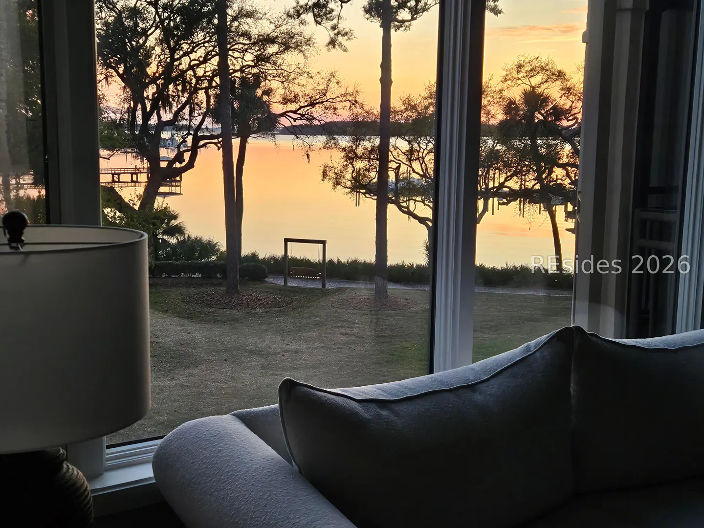 Living room view through a window of a sunset over a lake with trees and a swing.