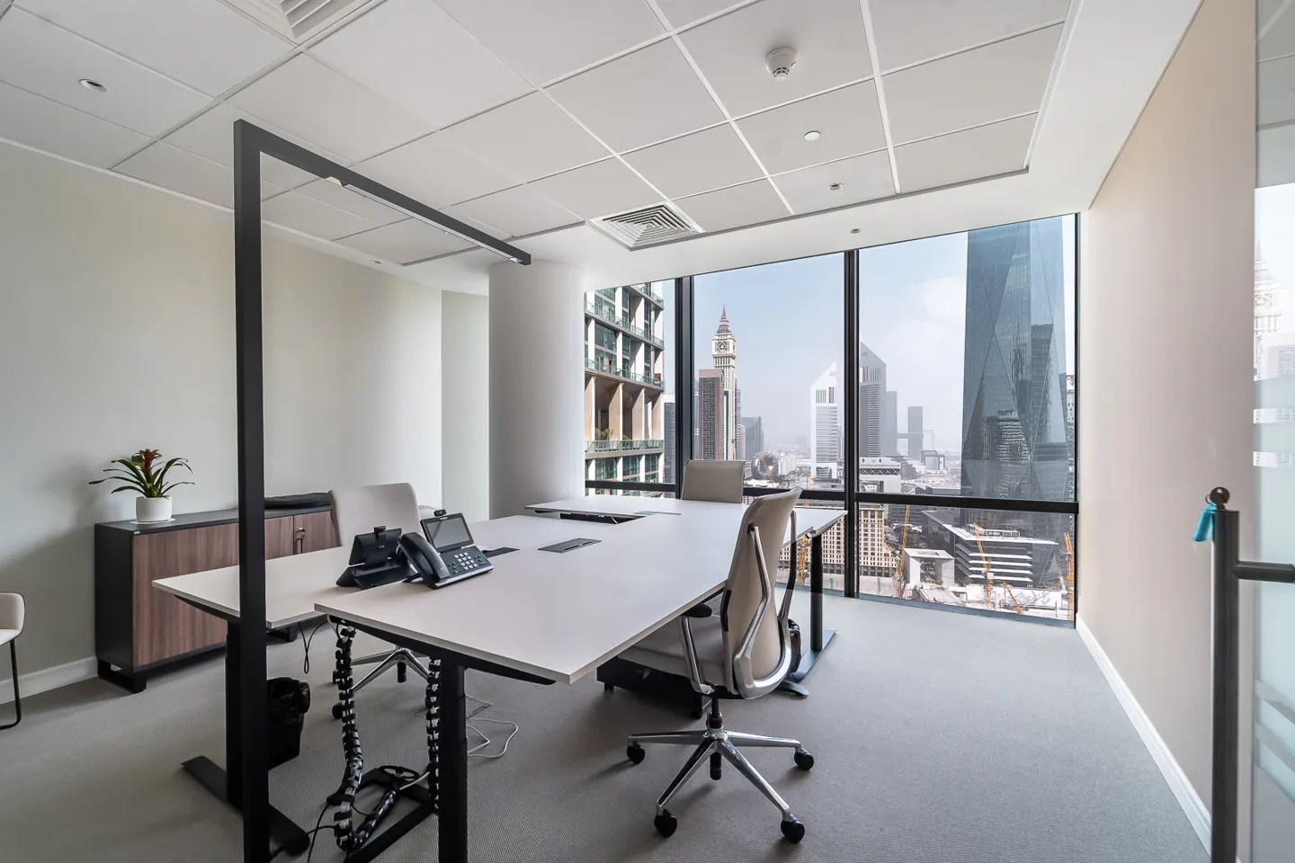 Bright office space with a white desk, ergonomic chair, and large window overlooking a city skyline. A black lamp stands over the desk.