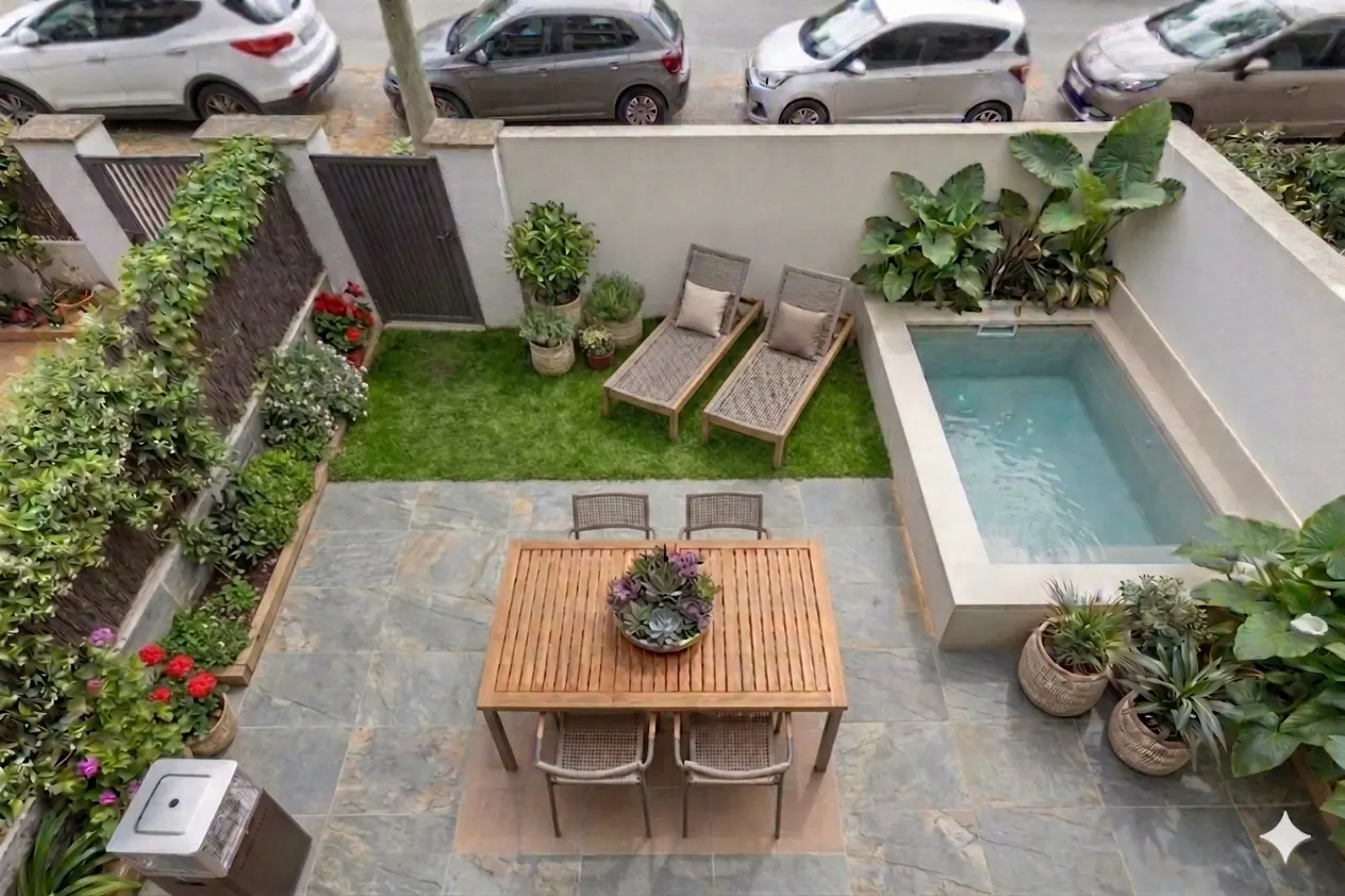 Overhead shot of a backyard with a small pool, lawn, lounge chairs, and a wooden table with four chairs. The yard is surrounded by a stone patio and lush greenery.