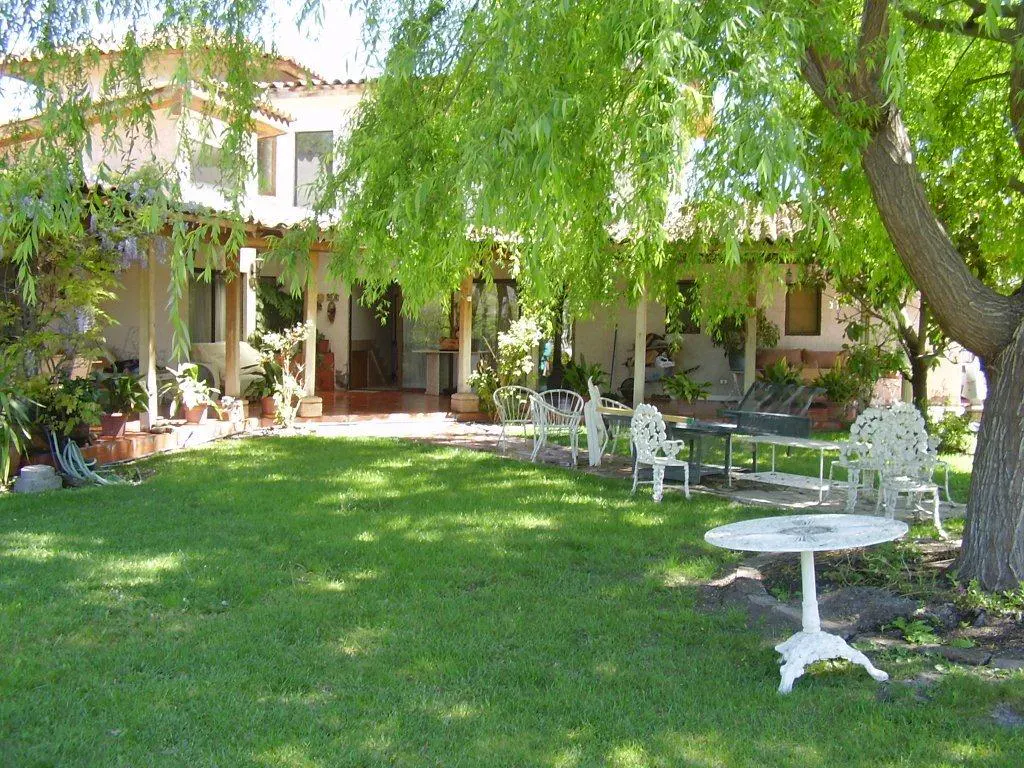 A two-story house with a green lawn and white outdoor furniture. A large tree provides shade.
