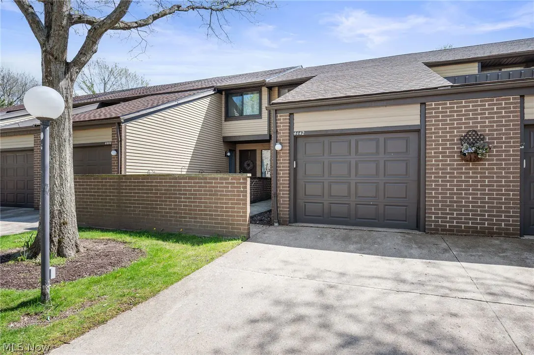 A two-story townhouse with a brown garage door and brick accents. A concrete driveway leads to the garage.