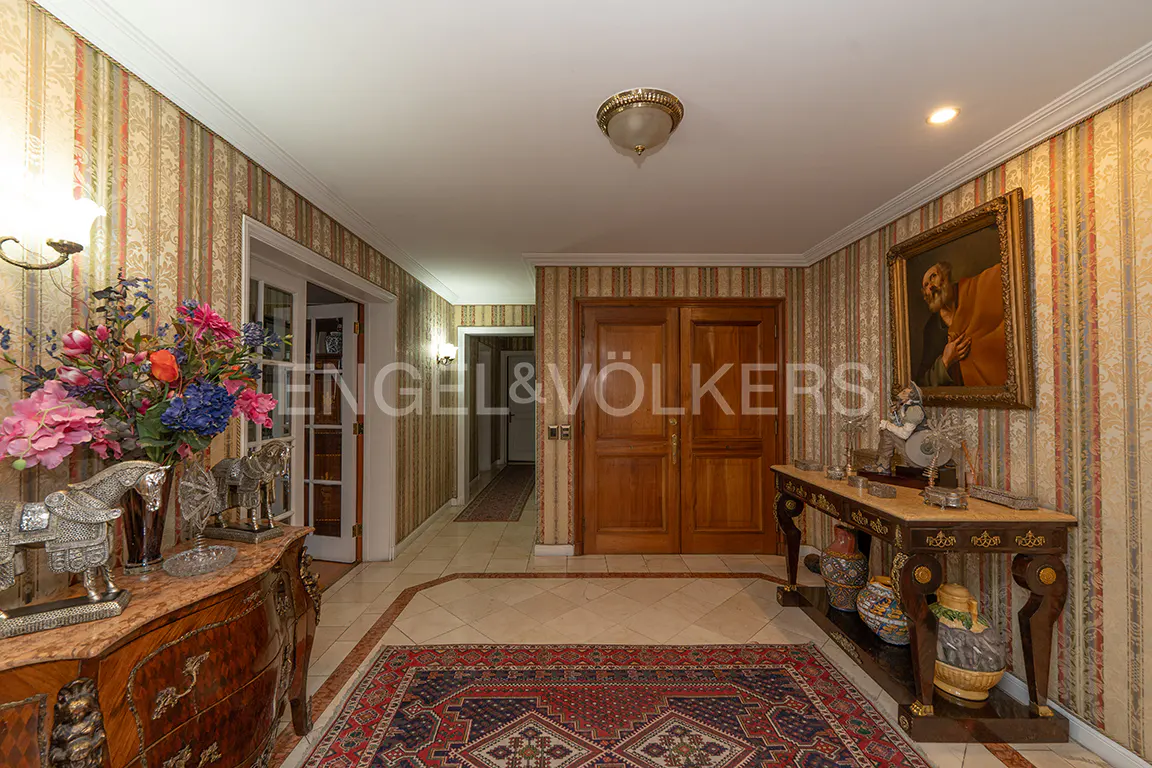 A foyer with striped wallpaper, a red and blue rug, and a wooden double door. A painting hangs on the right wall.