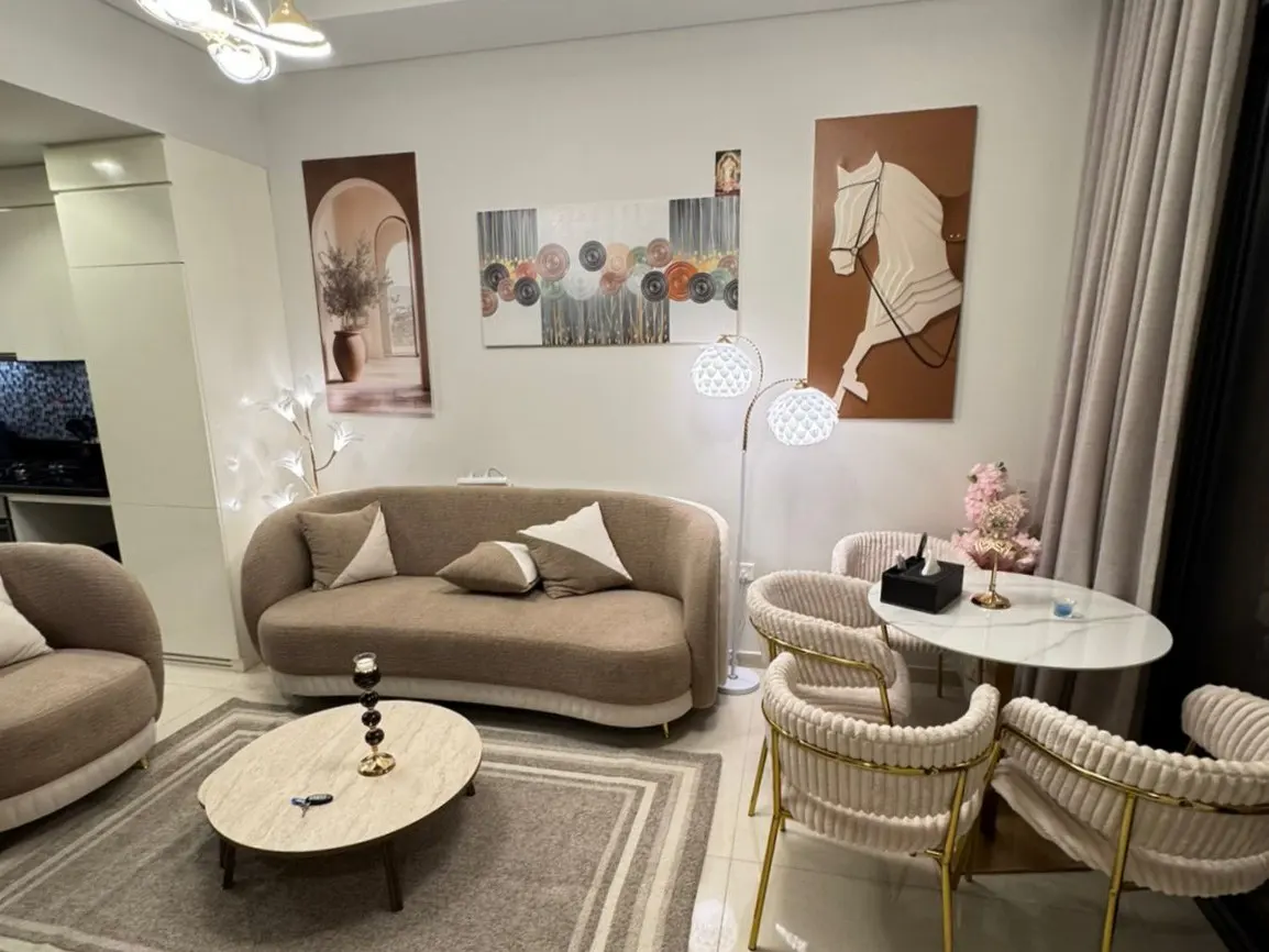 Living room with beige sofas, a marble coffee table, and a white dining table with four chairs. Artwork adorns the walls.