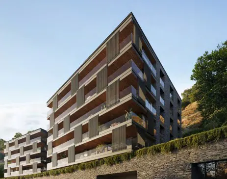 Modern apartment building with balconies, stone facade, and wood accents, set against a blue sky and hillside.