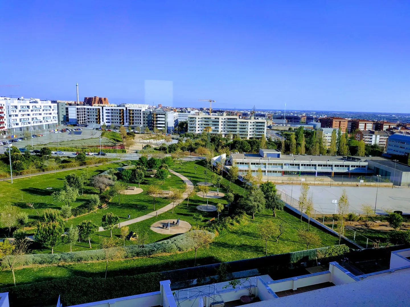 A high-angle view shows a green park surrounded by buildings under a clear blue sky.