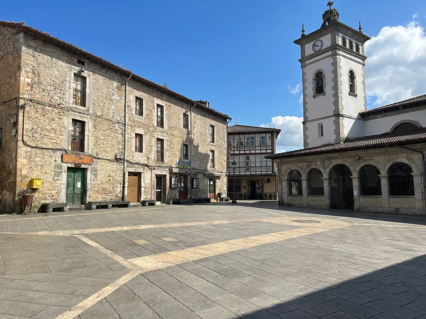 Town square with stone buildings, including a church with a clock tower, under a blue sky.