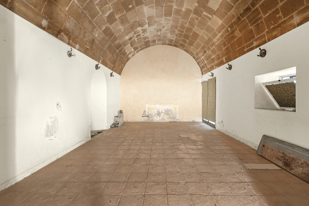 Empty room with a high, arched stone ceiling, white walls, tiled floor, and small wall-mounted hooks.