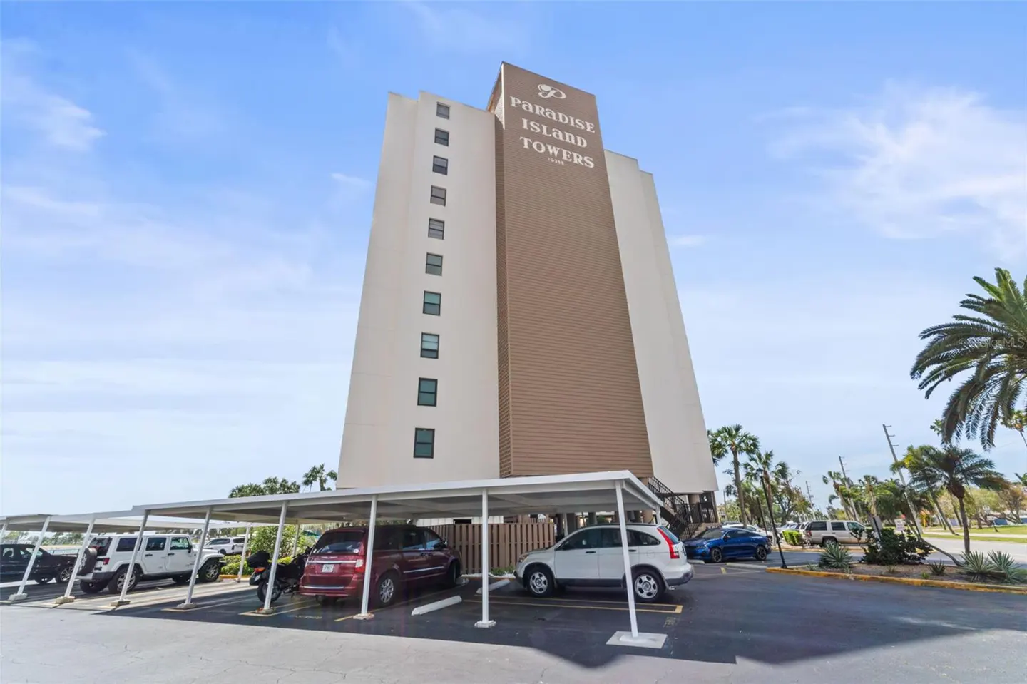 Exterior view of Paradise Island Towers, a tall beige and white building, with covered parking and cars in front.