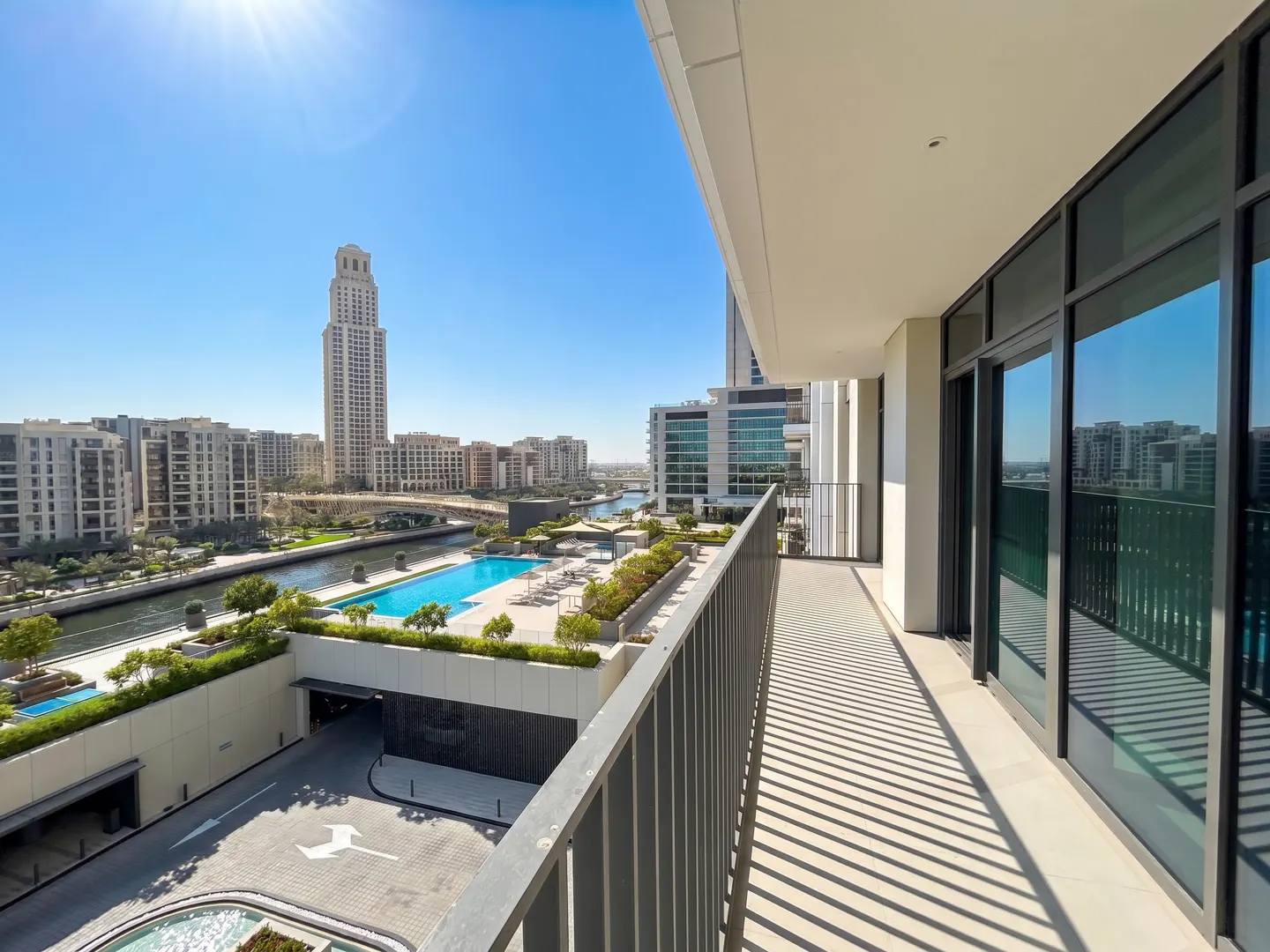 View from a balcony overlooking a city with a pool, river, and tall buildings under a clear blue sky.
