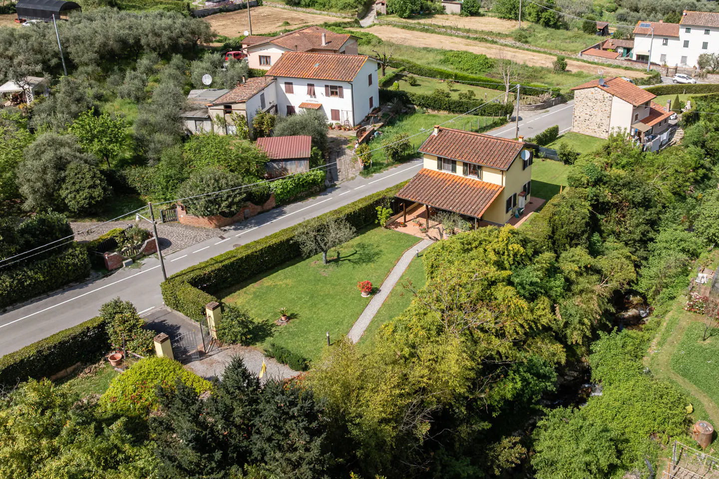 Aerial view of a yellow two-story house with a red tile roof, green lawn, and trimmed hedges in a rural setting.