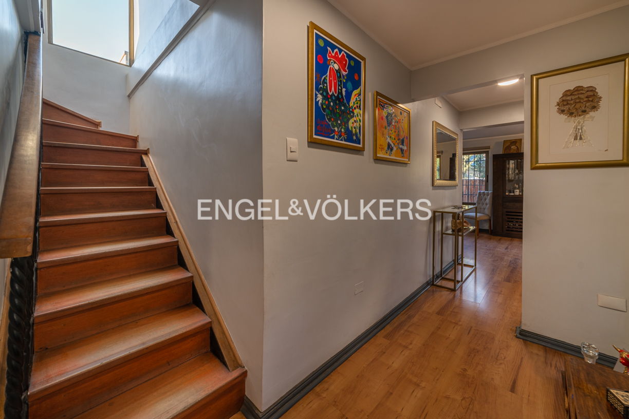 Wooden staircase in a hallway with light gray walls, colorful artwork, and hardwood floors leading to a dining area.