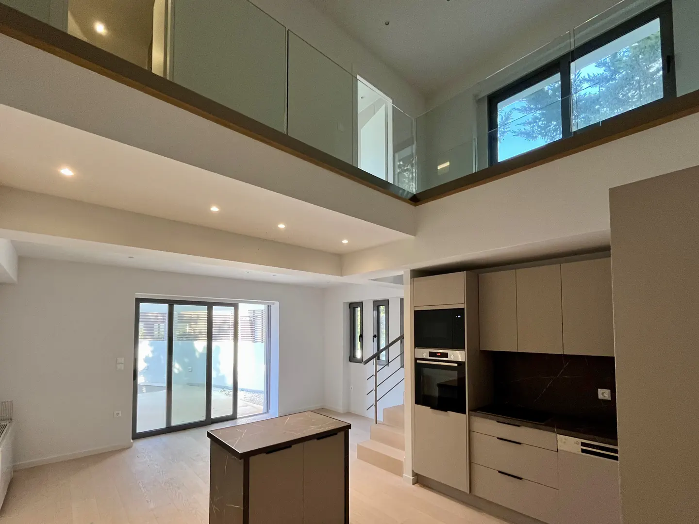 A bright, modern home interior with a kitchen island, light wood floors, and a second-story loft with glass railings.