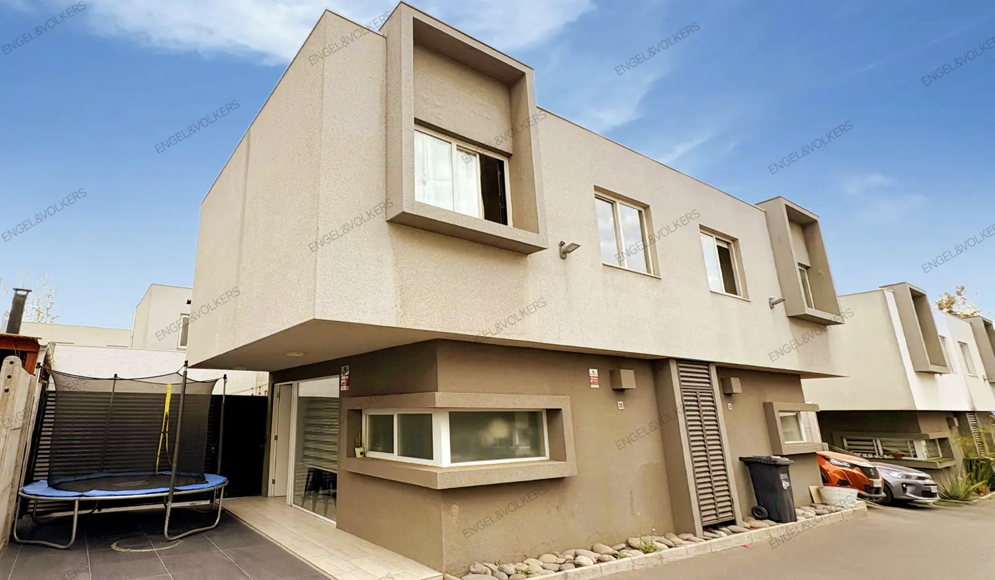 Modern townhouse exterior with beige stucco, rectangular windows, and a blue trampoline in the fenced yard.