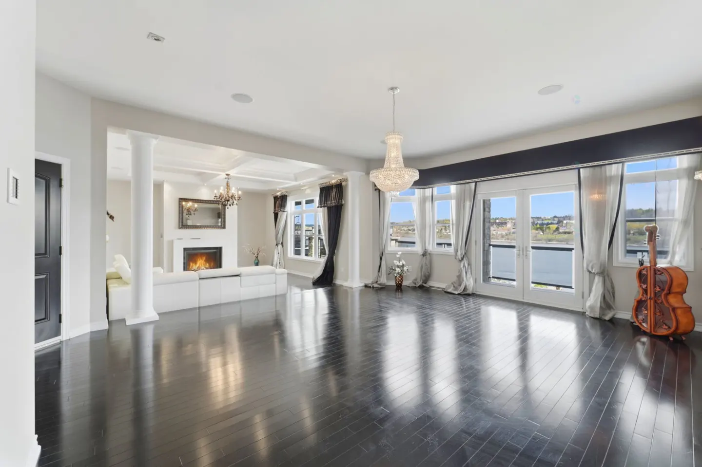 Spacious living room with dark hardwood floors, a crystal chandelier, white sofa, fireplace, and large windows with a view.