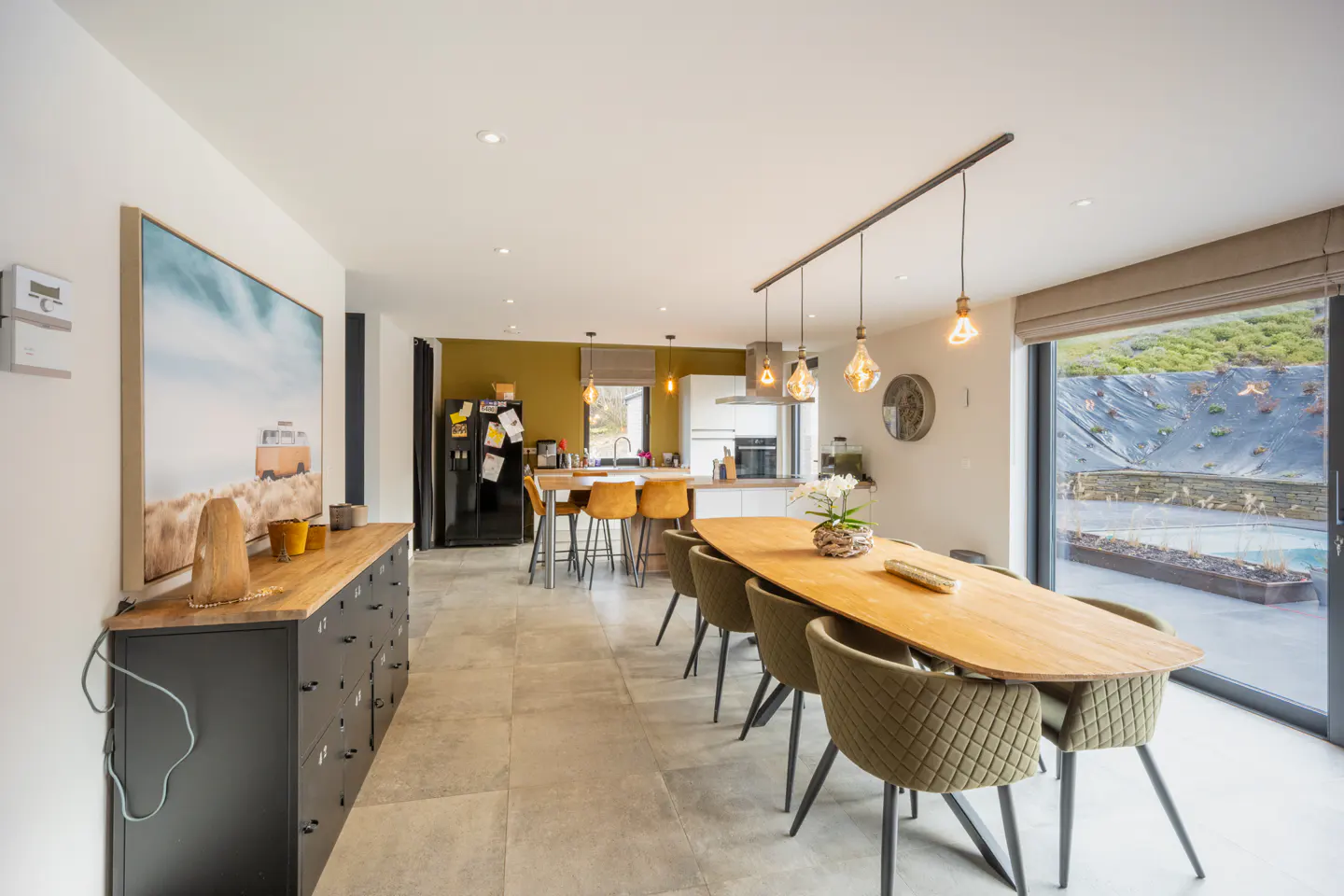 Open-concept kitchen and dining area with a long wood table, olive chairs, and a large sliding glass door to the backyard.