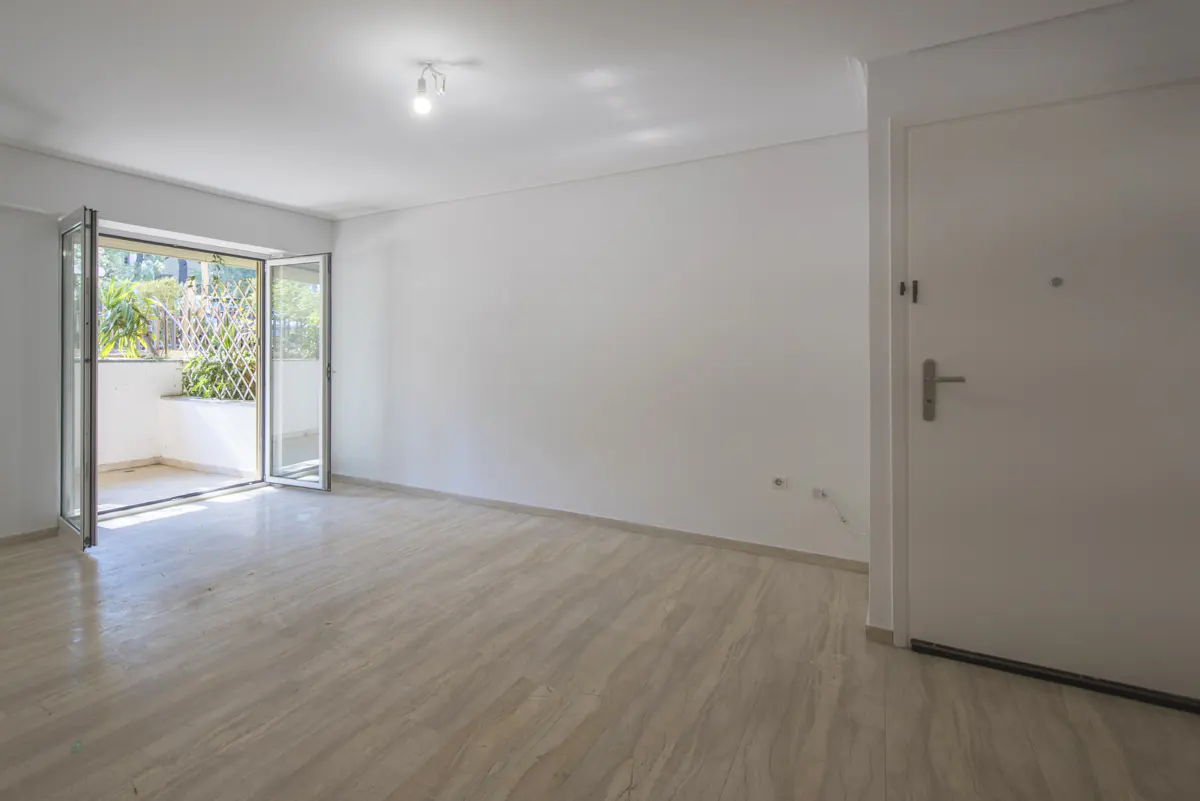 Bright, empty room with marble floors, white walls, and an open glass door to a balcony with plants. A white door is on the right.