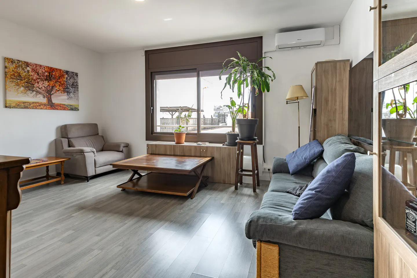 Living room with gray sofa, wood coffee table, and gray wood-look floors. A large window is above a low cabinet with plants.