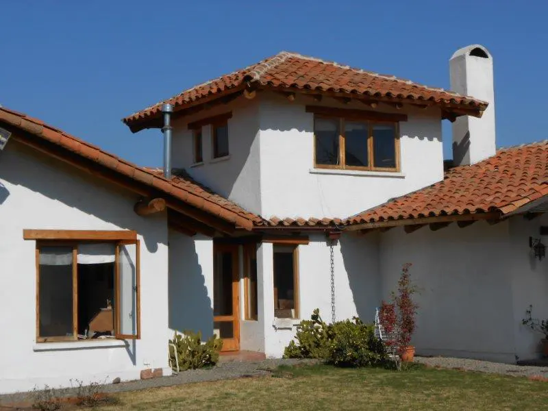 Exterior view of a white stucco house with a red tile roof and wooden window frames under a clear blue sky.