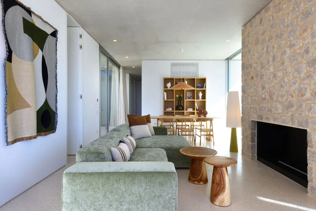 A bright living room with a green sofa, wooden tables, and a stone fireplace. An abstract art piece hangs on the wall.