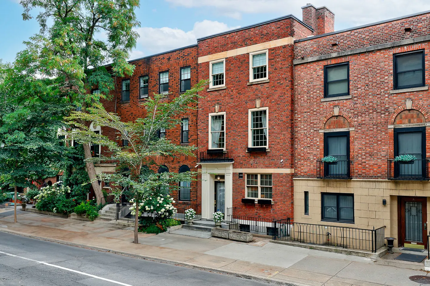 A row of red brick townhouses with black framed windows and green trees.
