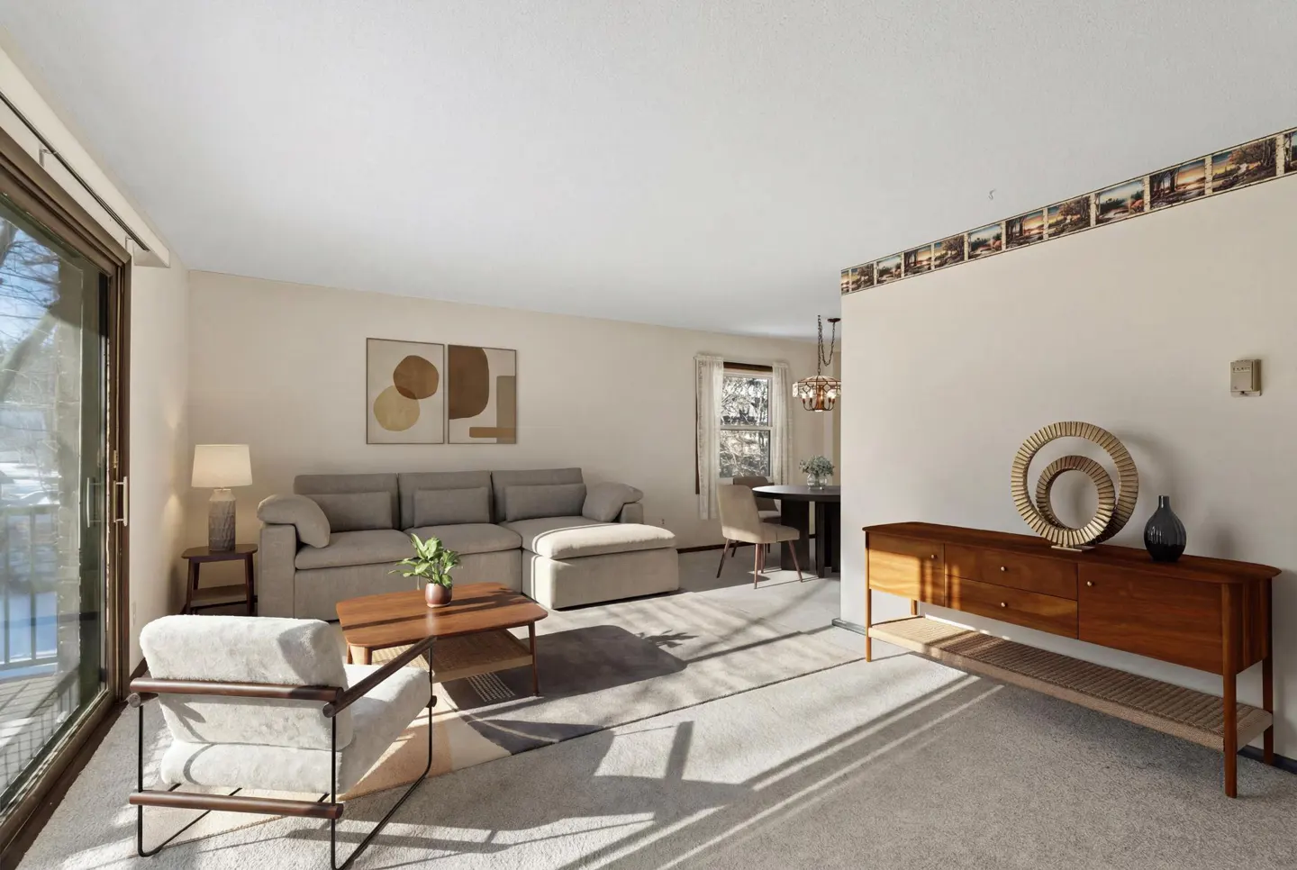 Living room with beige walls, carpet, and furniture. A gray couch, wood table, and chair sit on a rug. A wood cabinet is on the right.