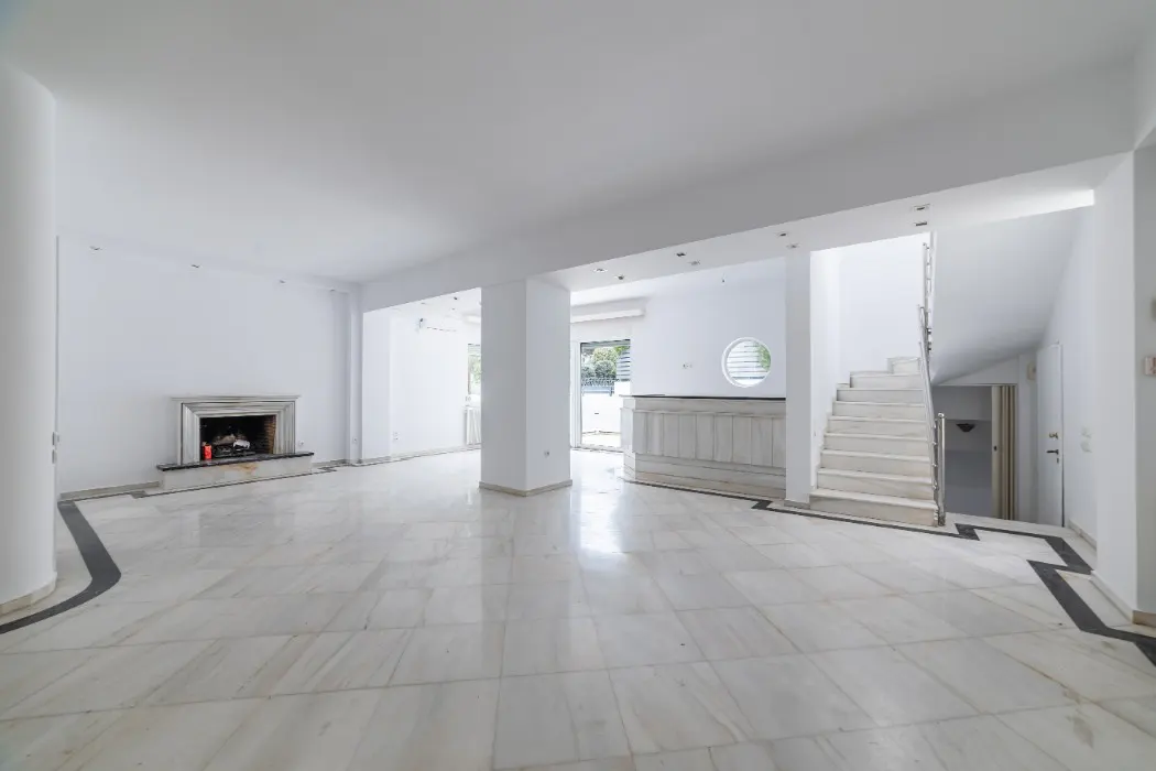 Bright, empty room with white walls, marble floors, and a fireplace. A staircase leads to an upper level.