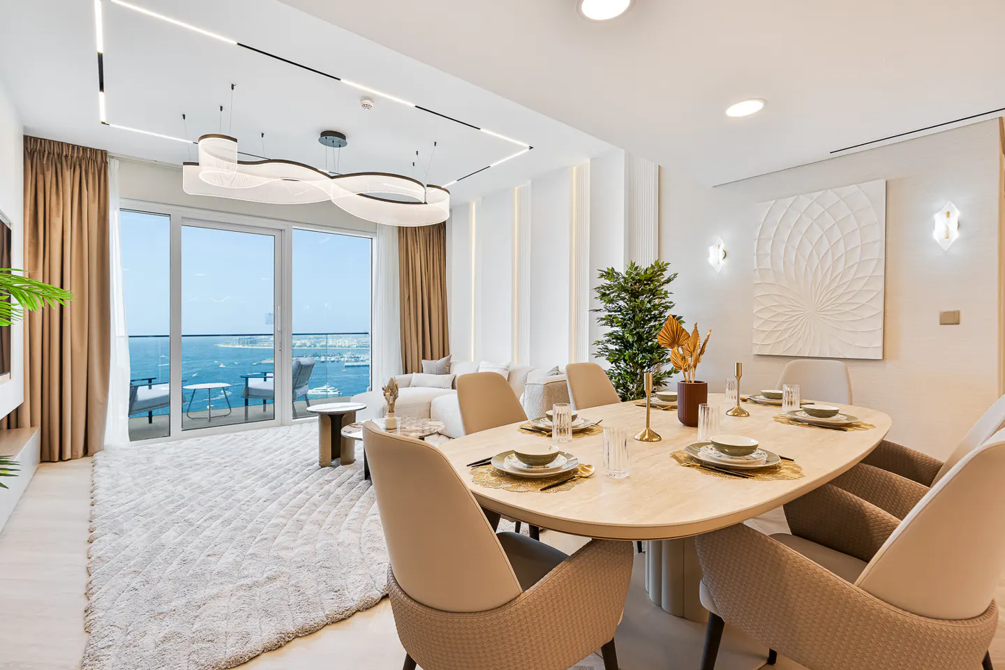 Bright, modern dining room with an oval table set for six, beige chairs, and a view of the ocean through large glass doors.