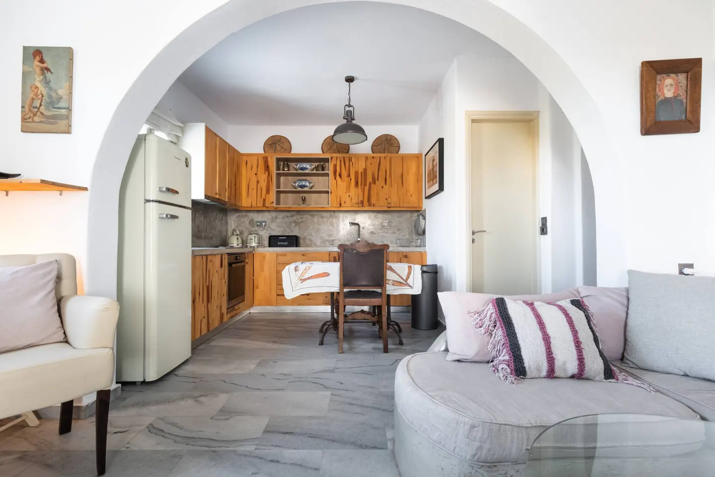 Open-concept living space with a kitchen, dining table, and sofa. The kitchen has wooden cabinets and a vintage-style refrigerator.