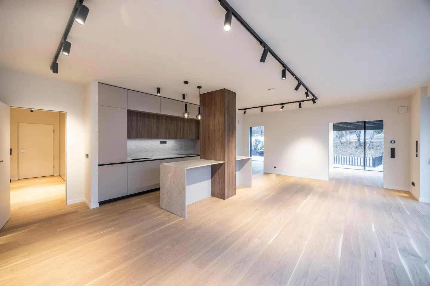 Bright, modern open-concept kitchen and living space with light wood floors. Gray cabinets, island, and track lighting.