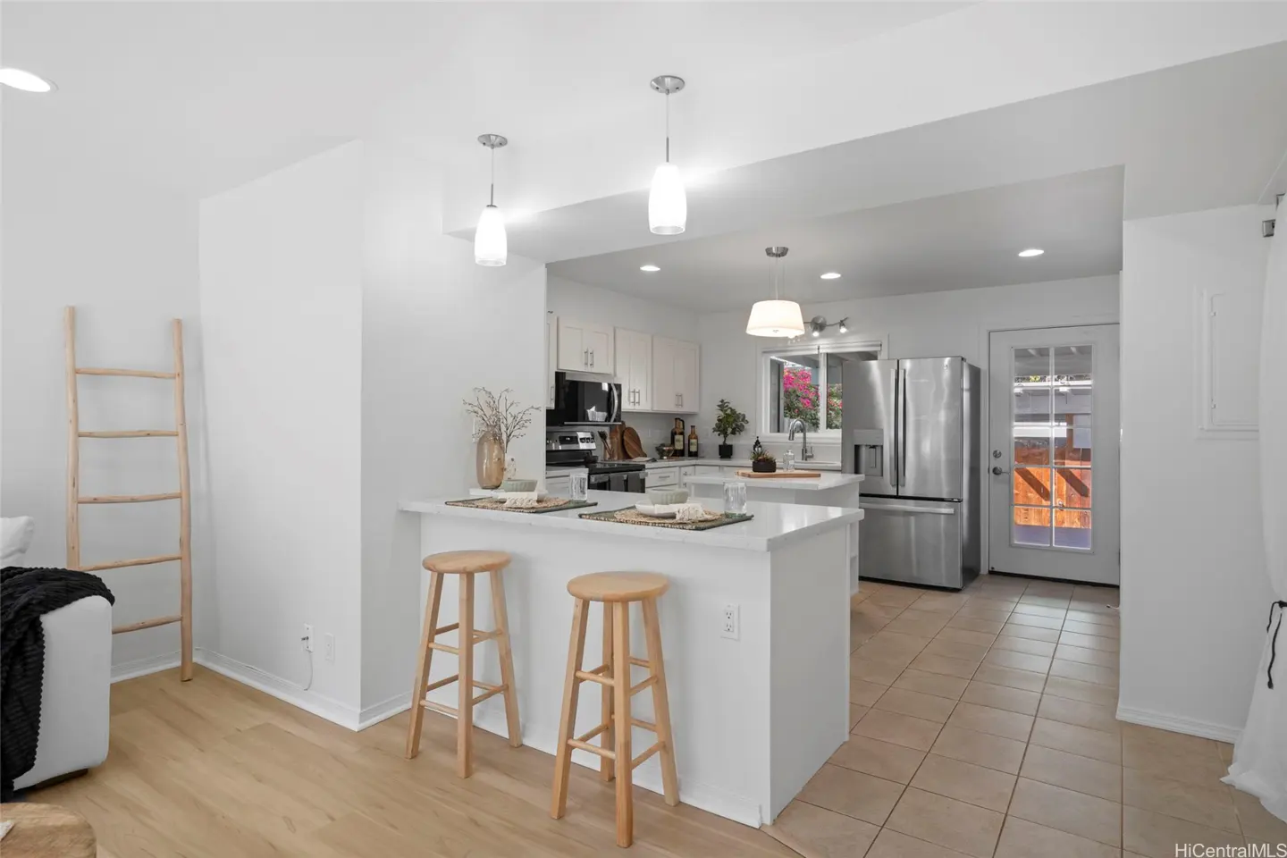 Bright, open kitchen with white cabinets, stainless steel appliances, and a breakfast bar with two wooden stools.