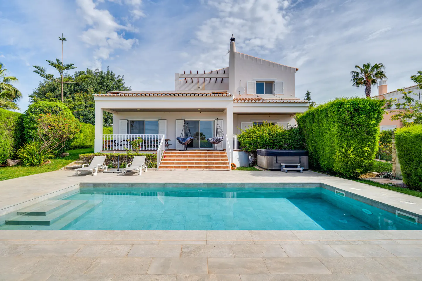 A two-story white house with a pool, lounge chairs, and a hot tub in the backyard.