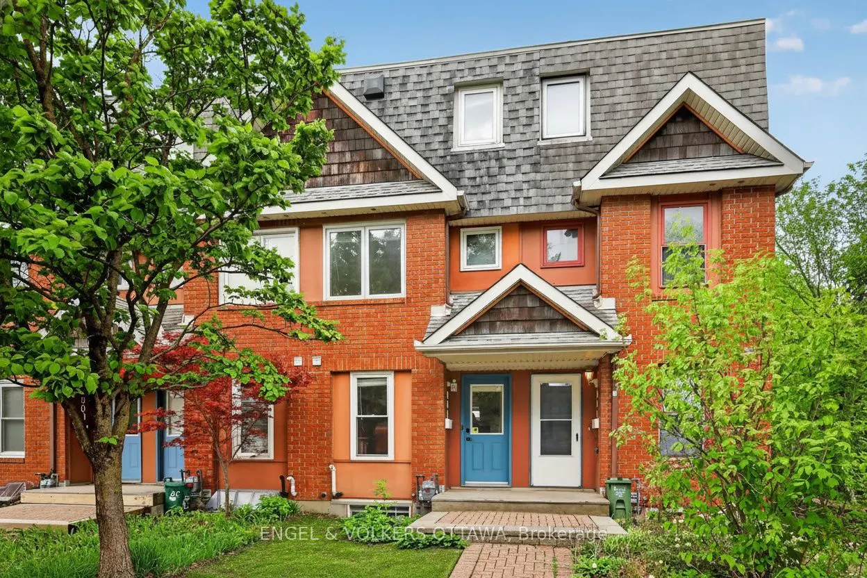 Exterior view of a red brick townhouse with a gray roof, blue and white doors, and green trees.
