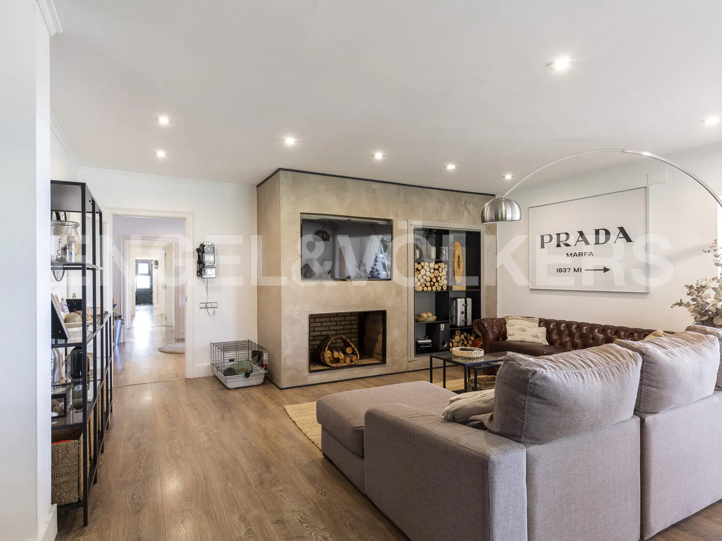 Modern living room with a grey sectional sofa, fireplace, built-in shelving, and a large Prada Marfa wall art piece.