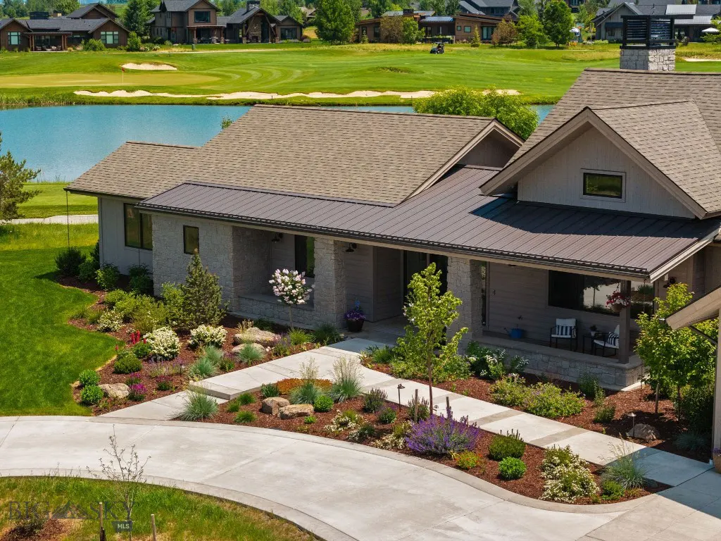 Exterior view of a gray house with a brown roof, a concrete driveway, and a green golf course in the background.