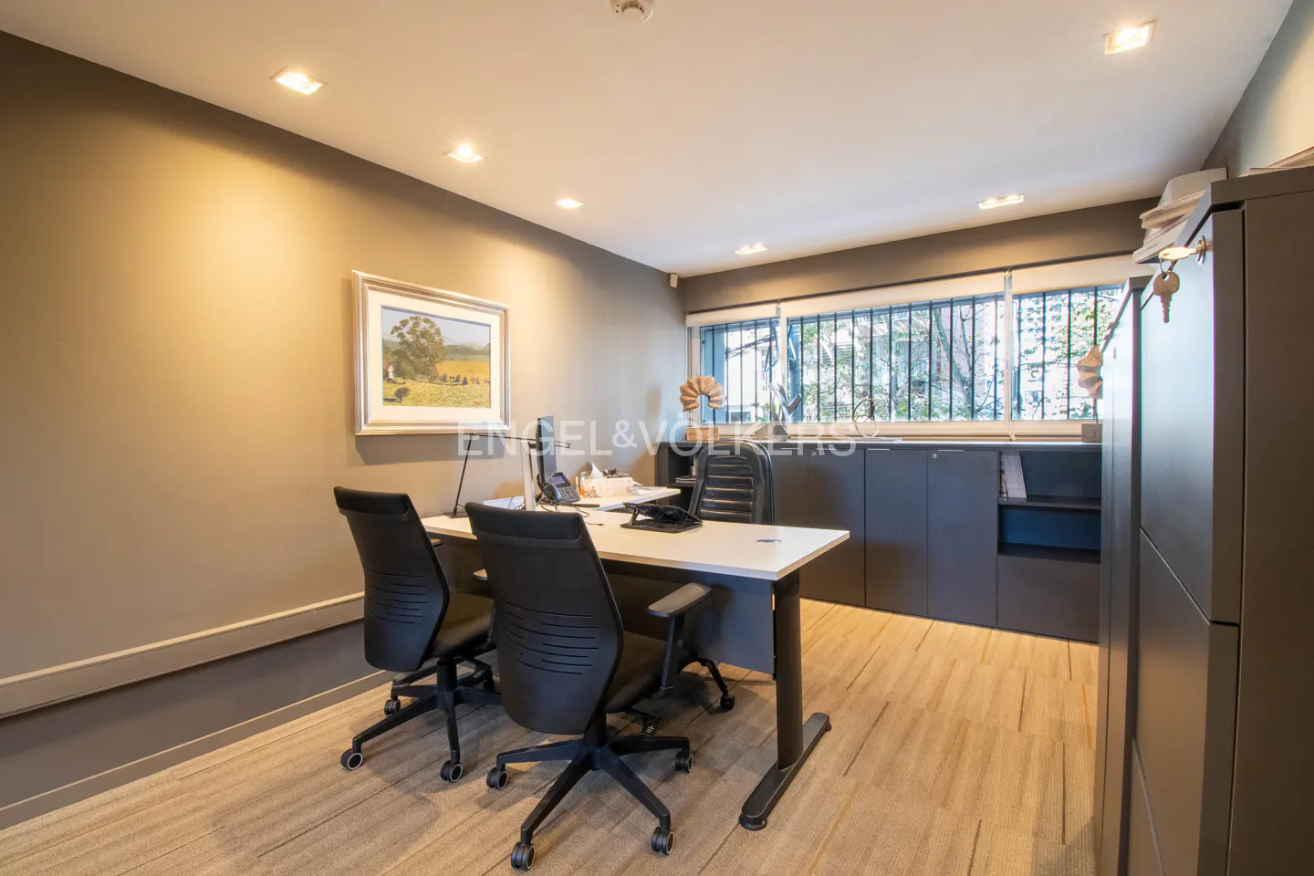 Office space with two black chairs at a white desk, gray walls, and a landscape painting.