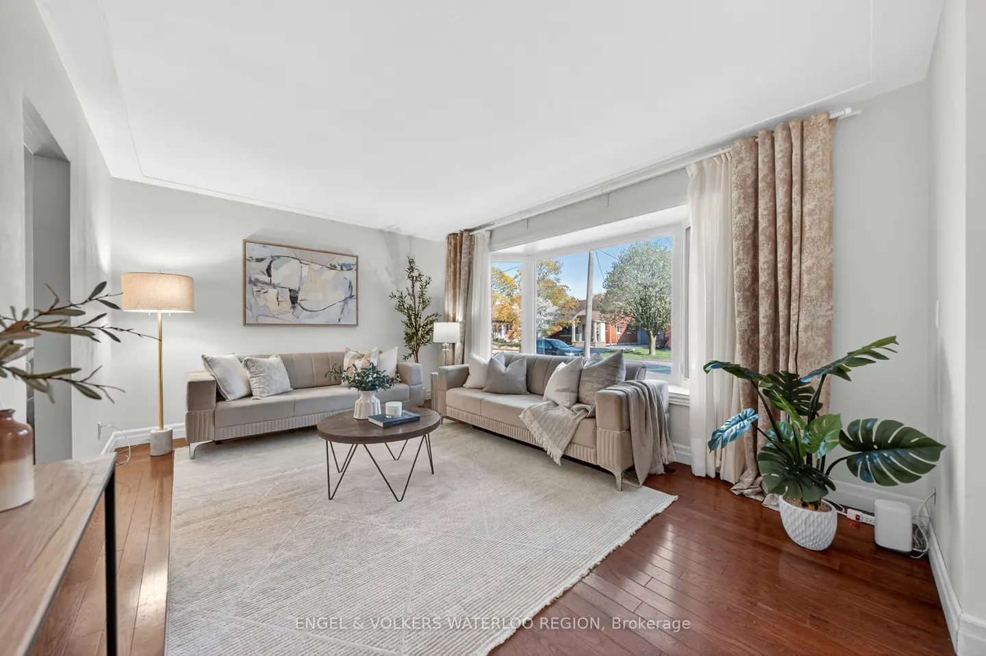 Living room with two beige sofas, a round coffee table, and a large window with patterned curtains.
