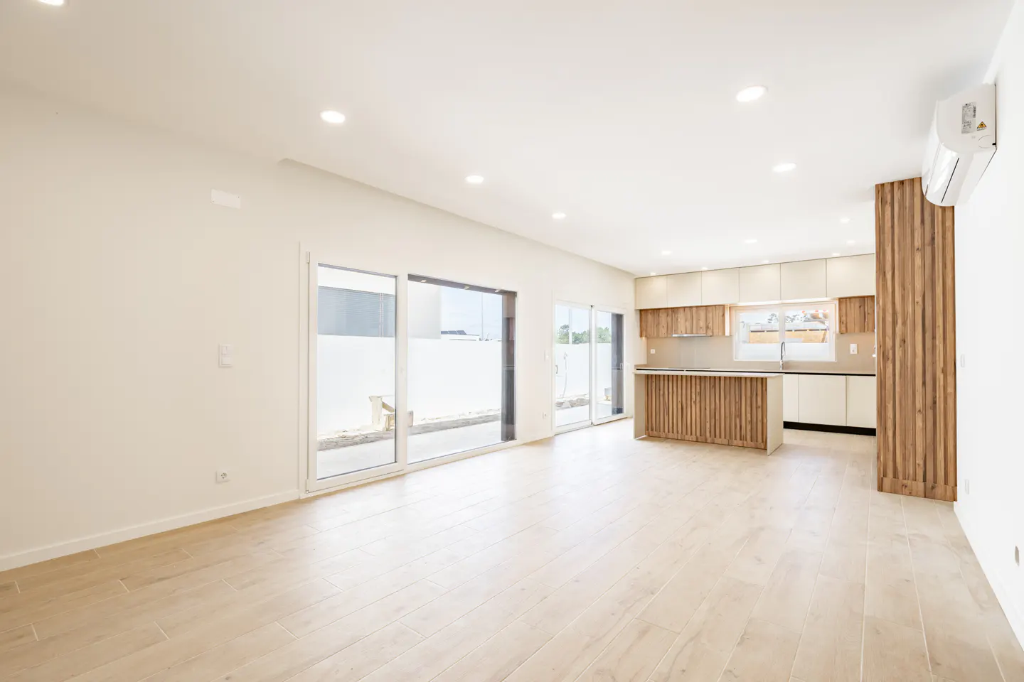 Modern open-plan living area with light wood floors, white walls, a kitchen island, and large sliding glass patio doors.