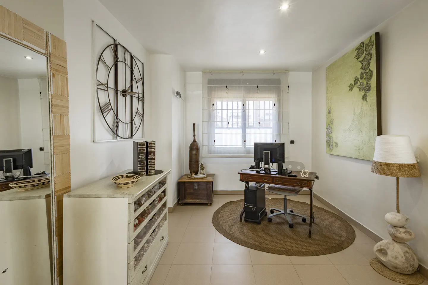 Bright home office with a wooden desk, computer, and a large clock on the wall. A unique lamp sits on stacked stones.
