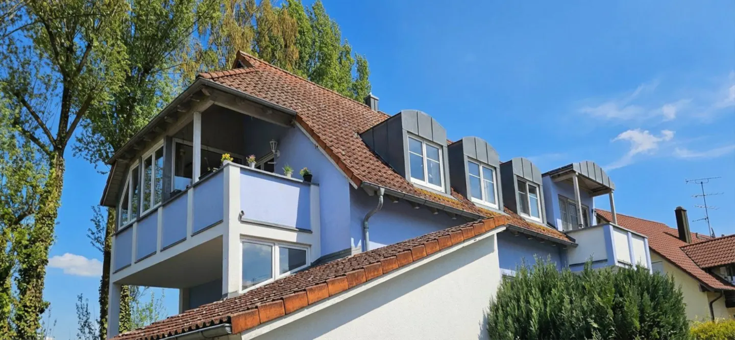 Exterior of a light blue house with a red tile roof and white trim under a blue sky.