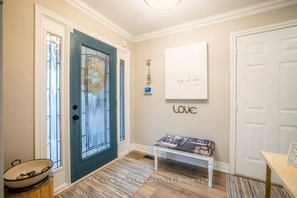 Foyer with a teal front door with glass panels, a white bench, and a white door. A white canvas with black text hangs on the wall.
